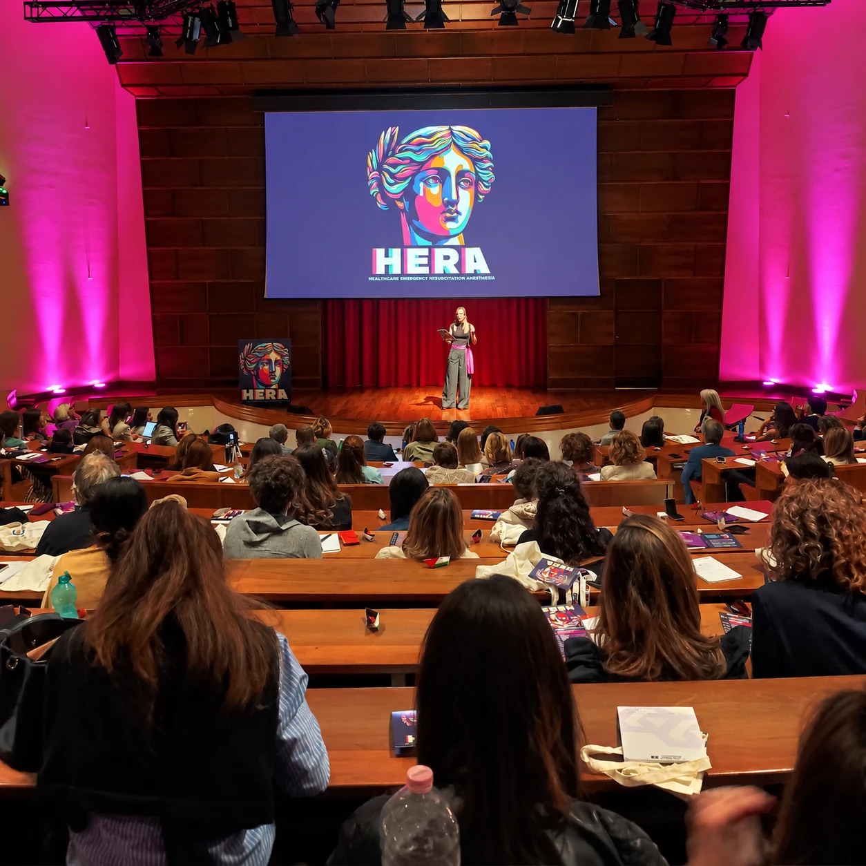 La sala di HERA Congress vista dalla platea, con una relatrice sul palco e il logo HERA sullo schermo