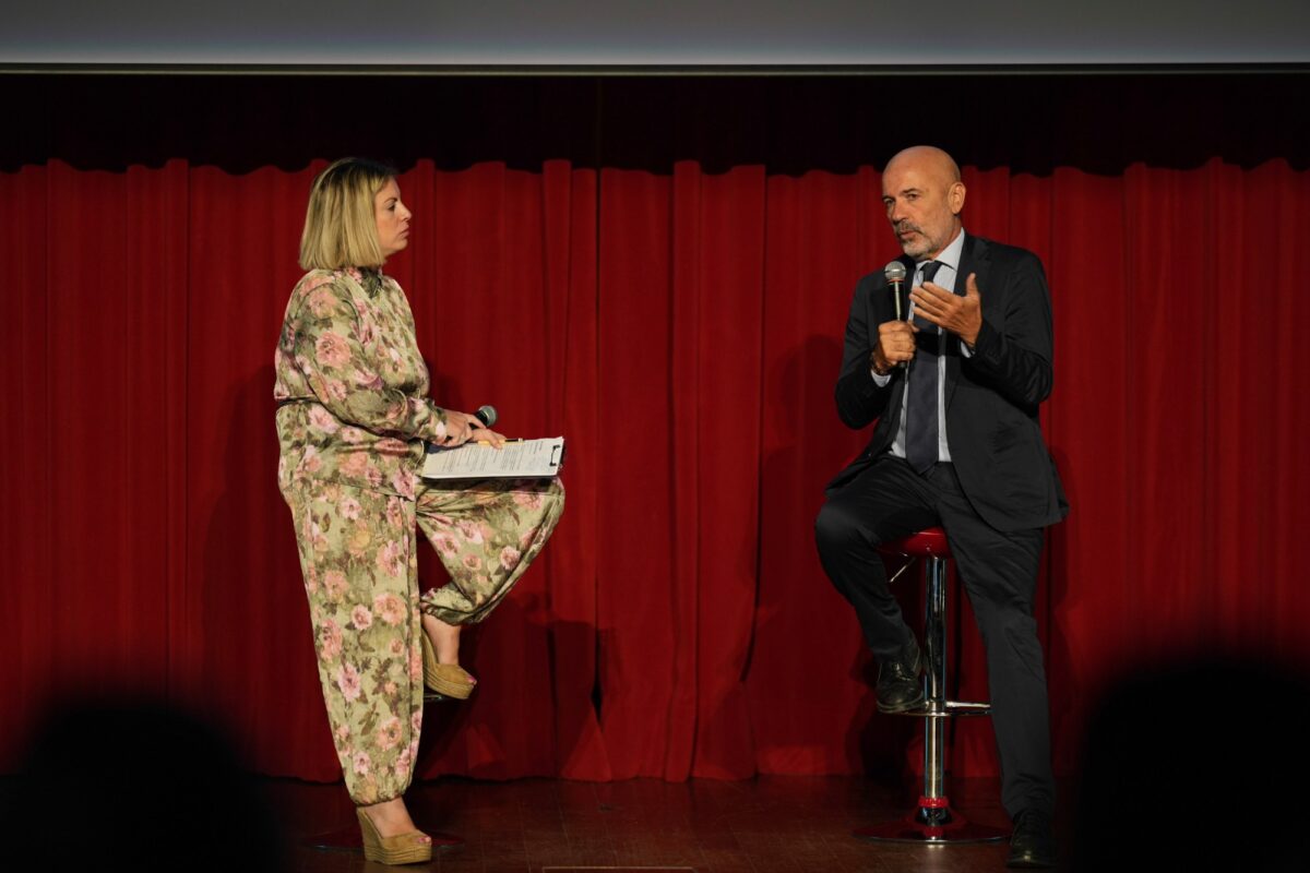 Angelo Aliquò e Chiara Gori seduti sul palco di HERA Congress 2026, davanti a un sipario rosso, durante l'intervista