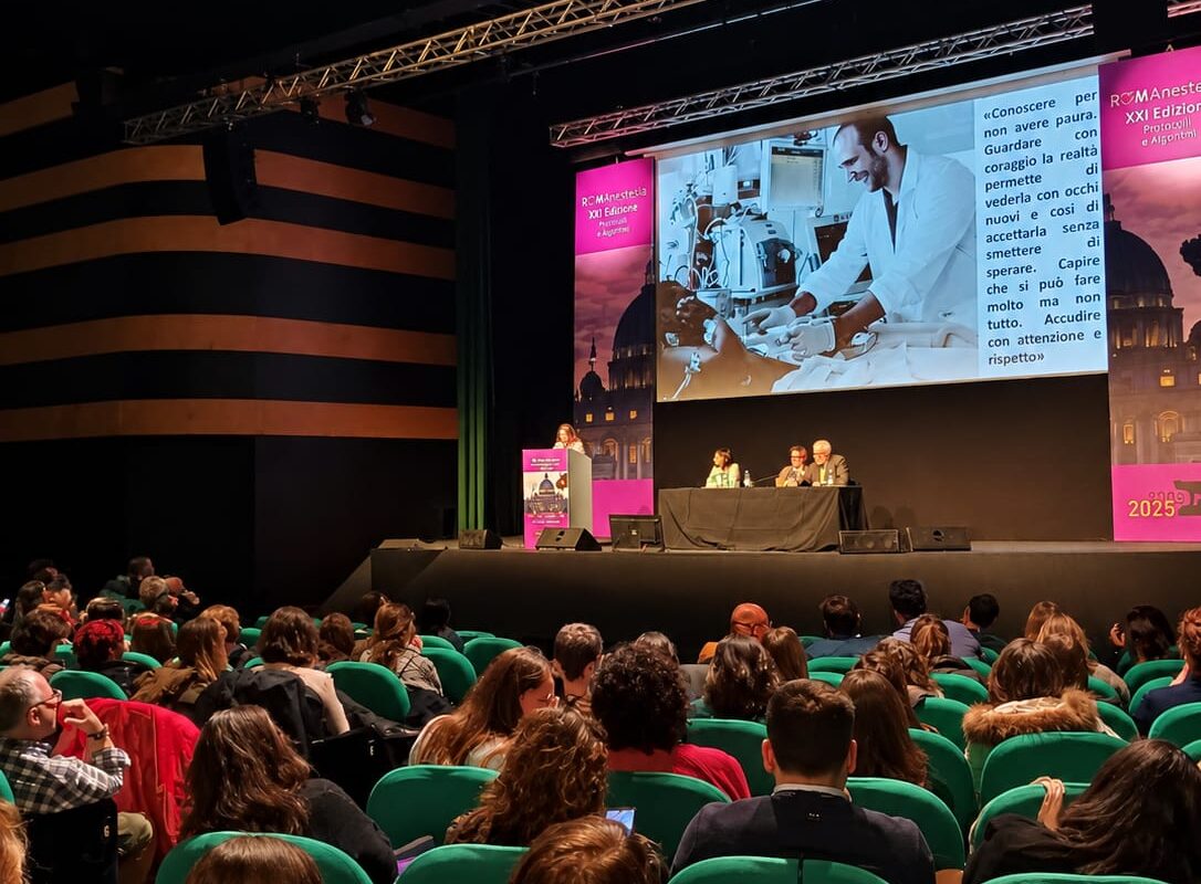 La platea di Romanestesia davanti al palco, con una relatrice al leggio e una slide sullo schermo