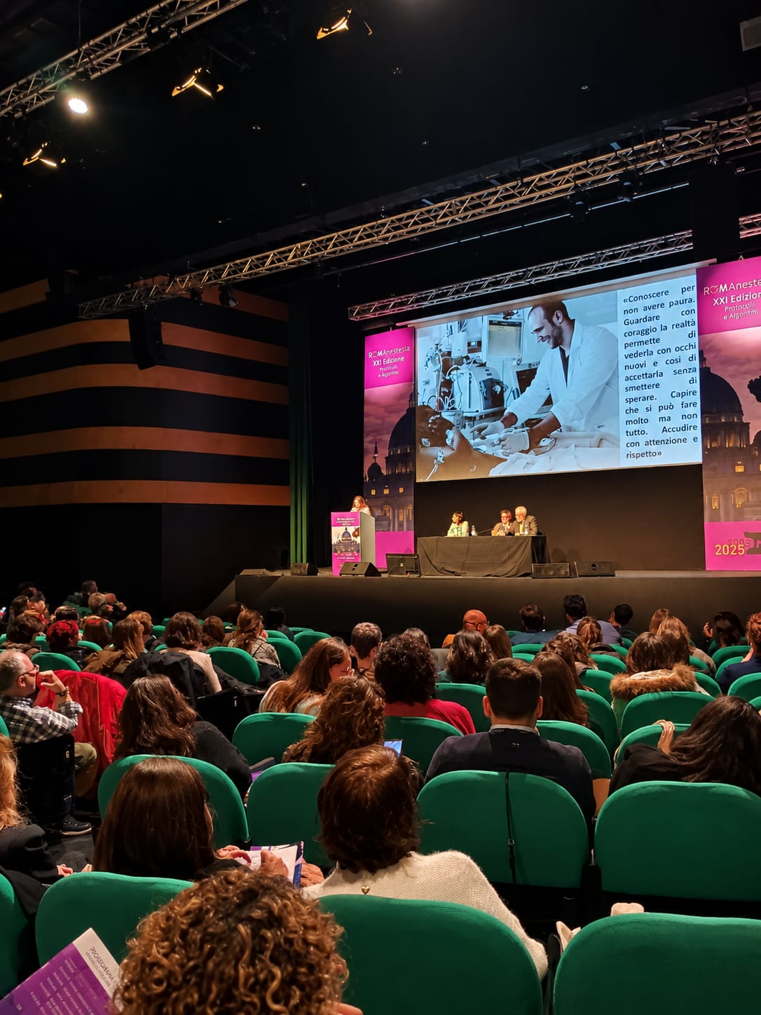 La platea di Romanestesia davanti al palco, con una relatrice al leggio e una slide sullo schermo